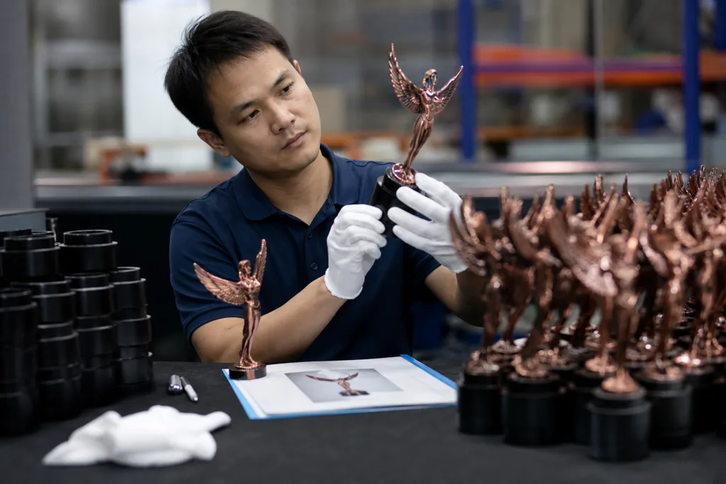 Quality inspector checking painted metal trophy finish consistency against an approved sample