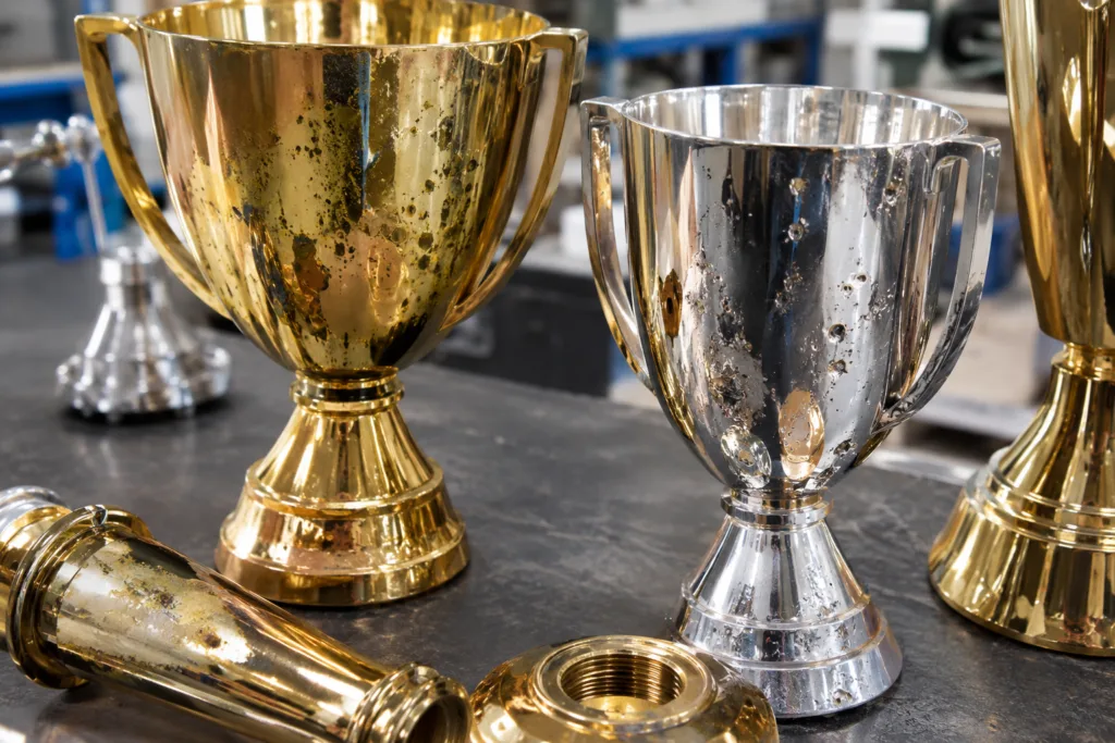 Electroplated Trophy Defects: Inspection Guide for Pitting, Blistering, and Color Variation 2 Metal award components showing pitting blistering and color variation for inspection